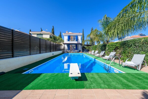 Une piscine avec un espace de détente, un bâtiment à deux étages et une clôture.