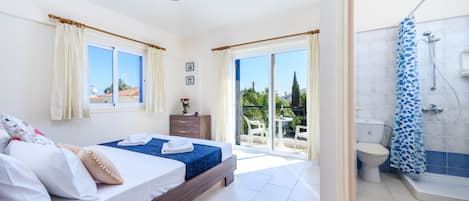 A bedroom with a bed, a dresser, and a window with curtains. There is a bathroom with a shower and a toilet.