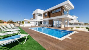 Una casa moderna de dos pisos con piscina, mobiliario exterior y césped bien cuidado.