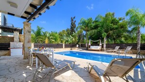 A pool area with lounge chairs, a stone floor, and tropical plants. - Villa Greco Mare 40 (Paralimni)