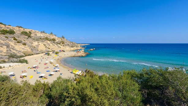 A beach with clear blue waters, sandy shore, and rocky hills in the background. - Villa Greco Mare 40 (Paralimni)