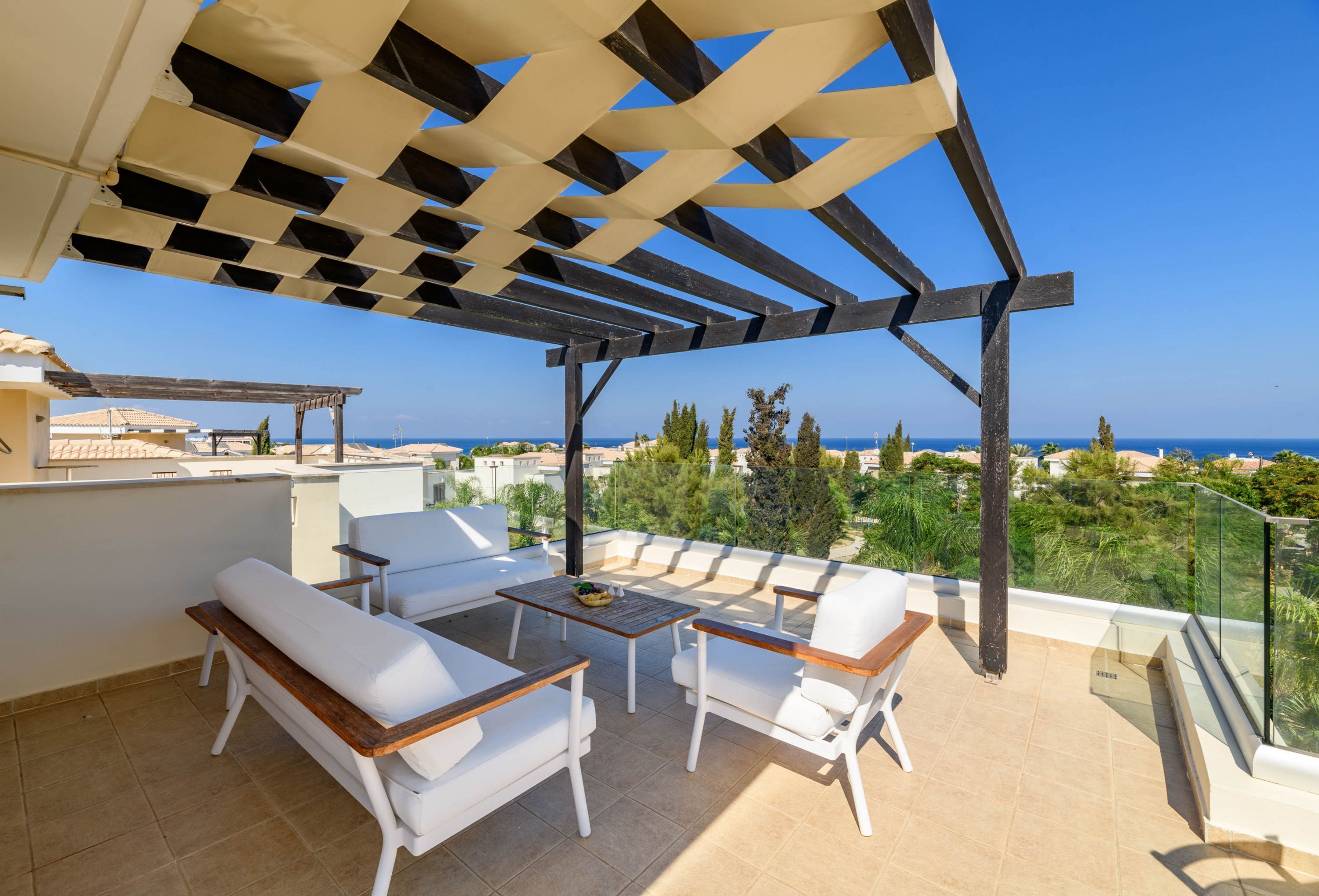 Una terraza con mobiliario blanco, una pérgola y vistas al mar.
