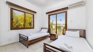 A hotel room with two single beds, a wooden headboard, a small bedside table, and a large window with a view of trees. - Villa Sam in Ayia Napa (Ayia Napa)