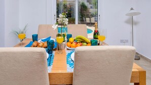 Un comedor con una mesa preparada para dos personas, que incluye una botella de champán, fruta y pasteles.