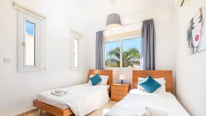 Habitación de hotel con dos camas, una ventana con cortinas, una mesita de noche con lámpara y un cuadro en la pared.