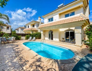 A residential property with a swimming pool, outdoor seating, and a tiled roof.