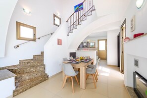 Un salón amplio con una mesa de comedor para cuatro, una cocina al fondo y una escalera que lleva a un piso superior.