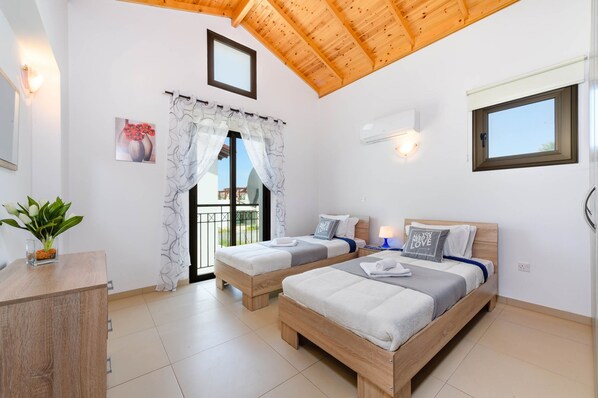 A bedroom with two wooden beds, a window with a view, a ceiling fan, and a small bedside table.