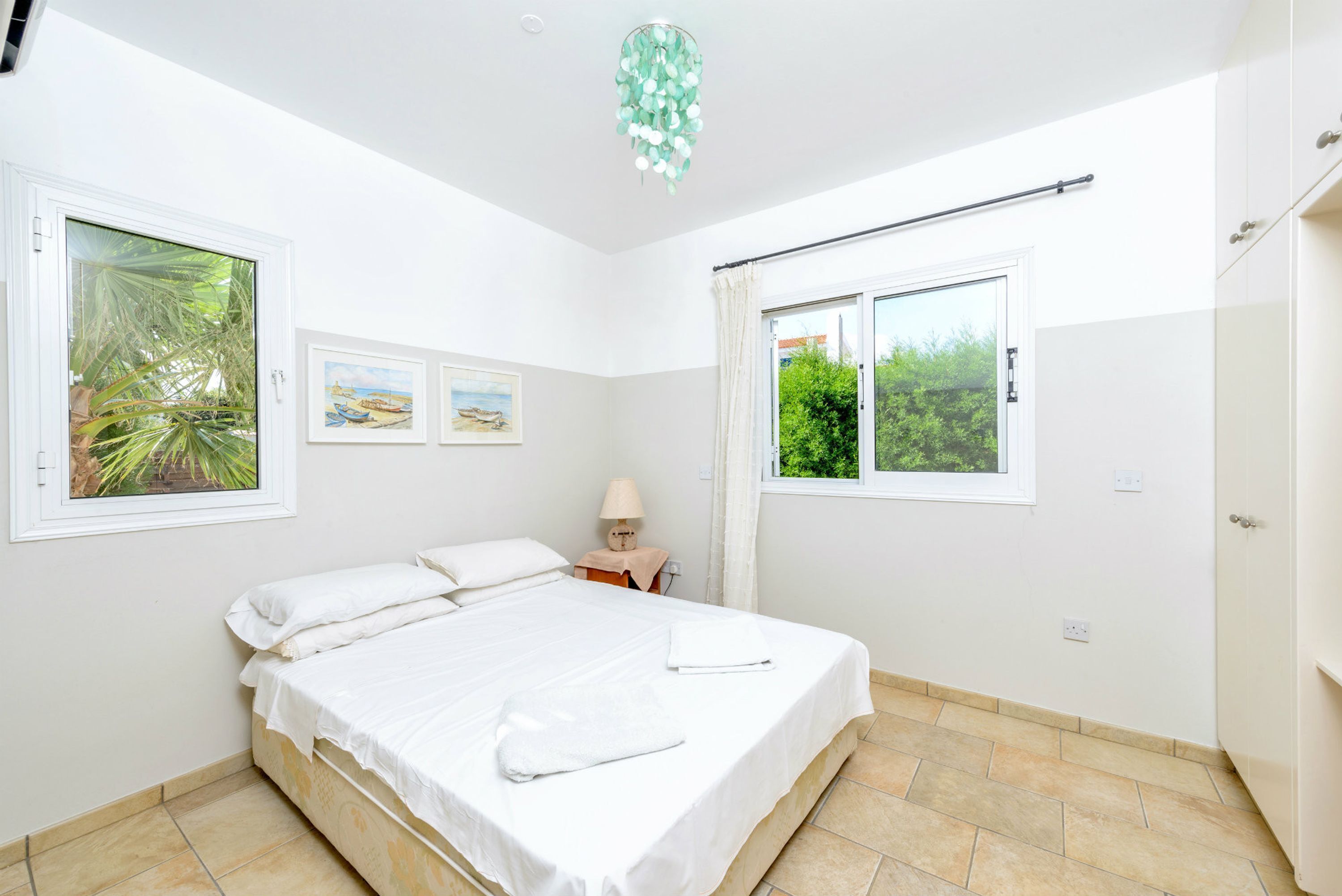 A bedroom with a bed, a nightstand, a lamp, and two windows with curtains.