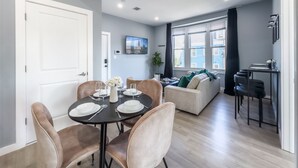 Un espace repas moderne avec une table ronde pour quatre personnes, un canapé et un petit coin cuisine équipé d’un téléviseur.