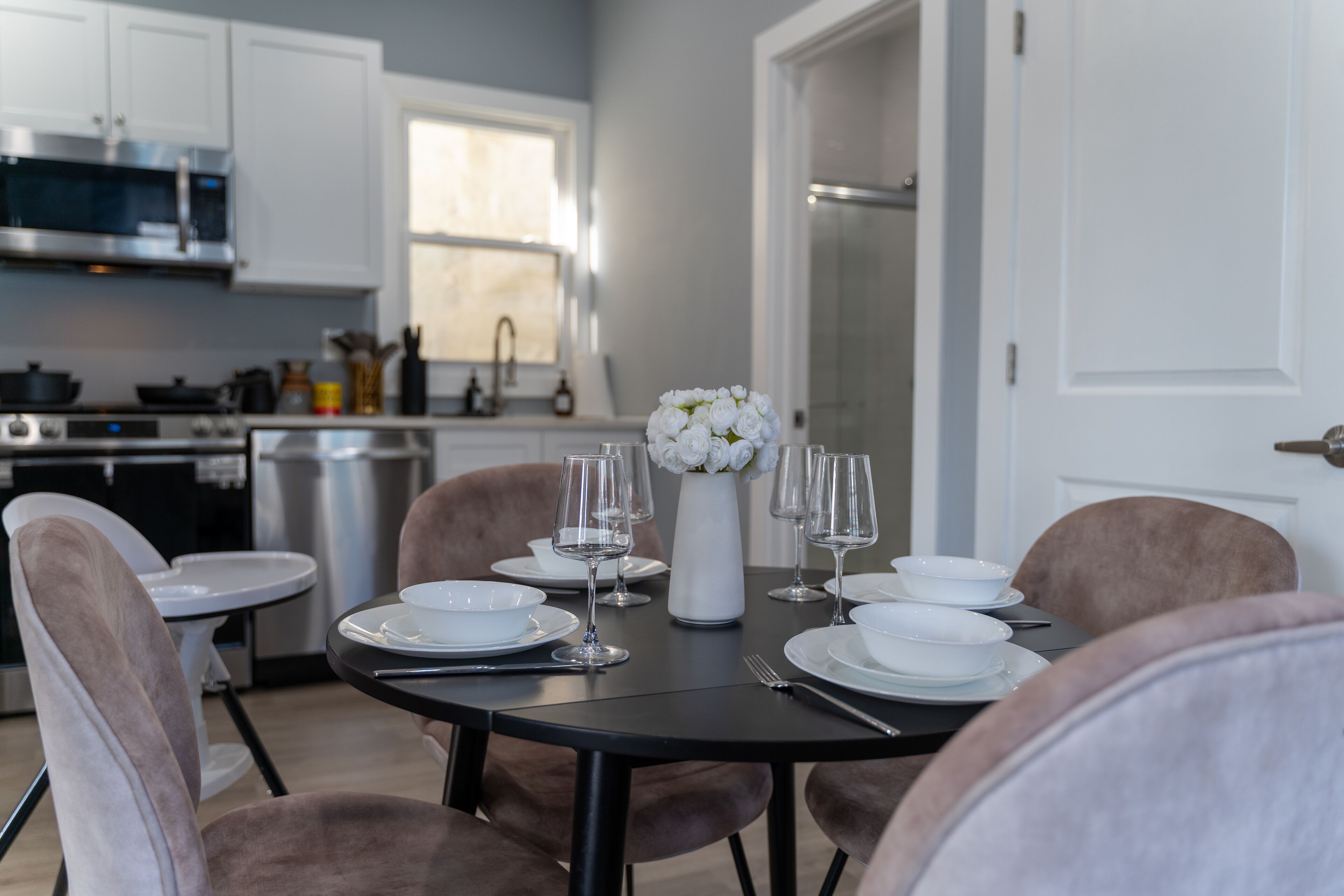 A dining area with a round table set for four, white plates, and clear wine glasses.
