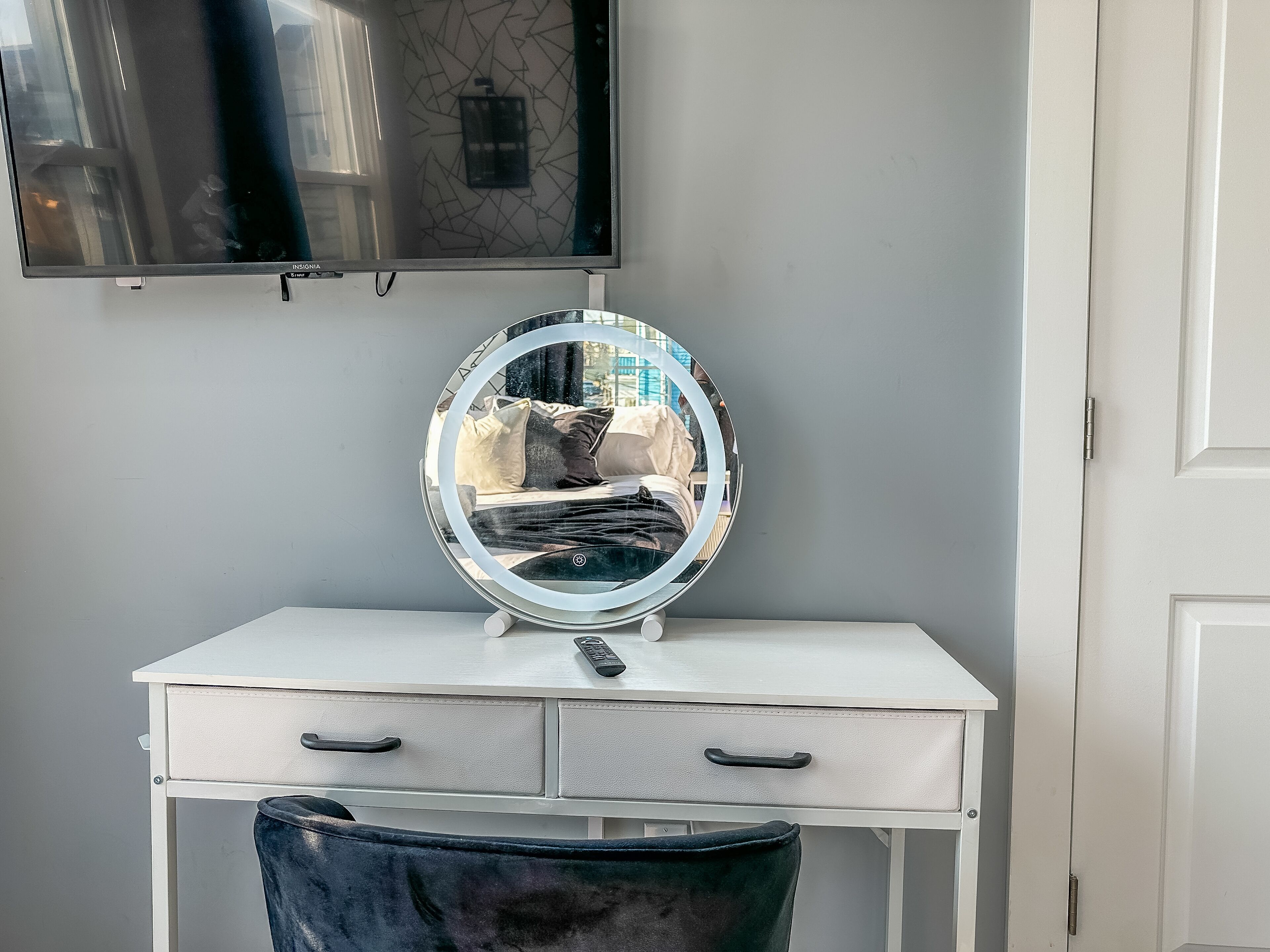 A white vanity with a round mirror, two drawers, and a remote control on the counter.