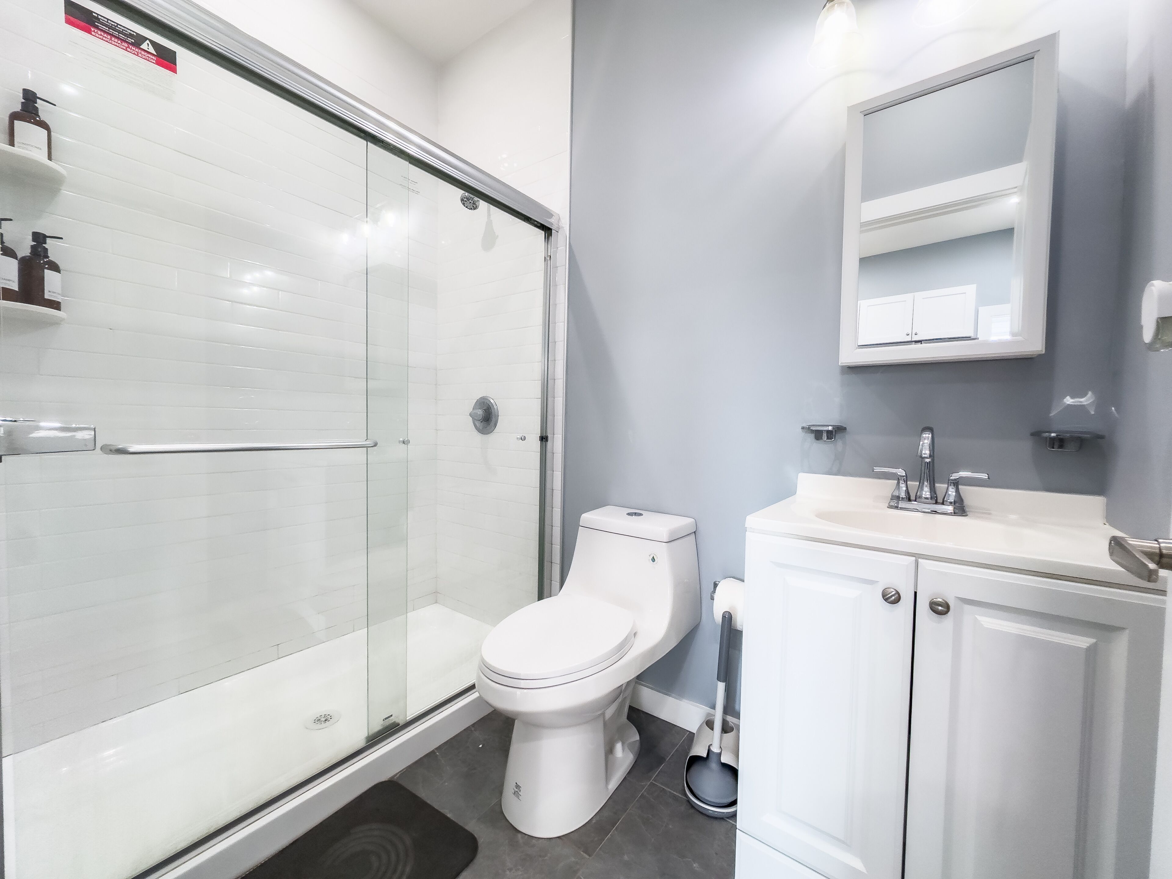 Ein modernes Badezimmer mit Duschkabine aus Glas, einer weißen Toilette und einem Waschbecken mit Spiegel.