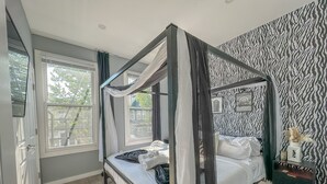 Un lit à baldaquin, un mur orné d’un motif zébré et une vue sur l’extérieur grâce à de grandes fenêtres.