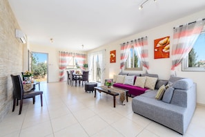 A spacious living room with a grey sofa, a dining table with chairs, and a coffee table. - Villa Marizan in Protaras (Paralimni)