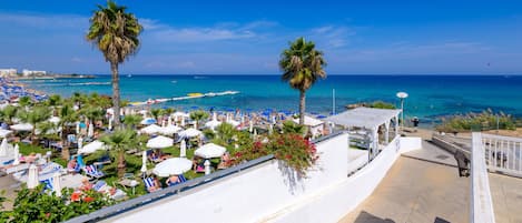 A beachside resort with sun loungers, umbrellas, and palm trees.