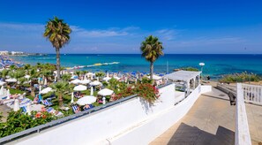 A beachside resort with sun loungers, umbrellas, and palm trees. - Villa Marizan in Protaras (Paralimni)