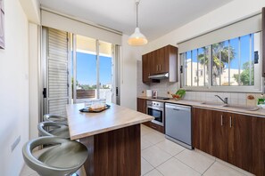 A modern kitchen with a central island, wooden cabinets, a built-in oven, and a dishwasher. - Villa Marizan in Protaras (Paralimni)