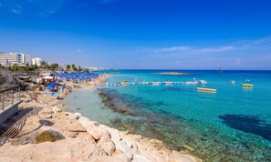 A beach with clear turquoise water, blue umbrellas, and boats.