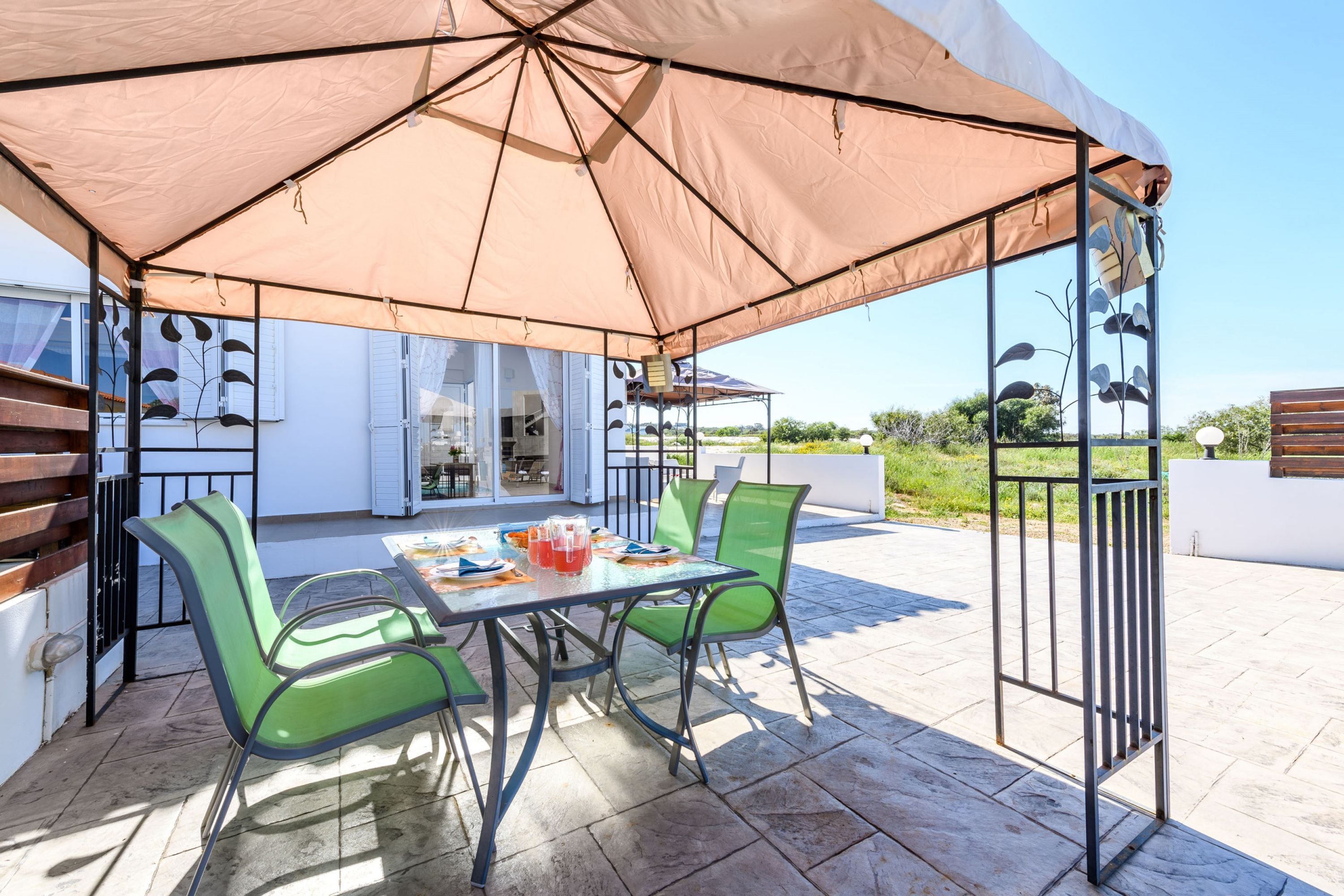 An outdoor patio with a table and chairs, a large umbrella, and a view of the surrounding area.