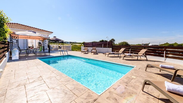 A rooftop pool with clear blue water, surrounded by lounge chairs and a pergola. - Sunset Villa in Protaras (Paralimni)