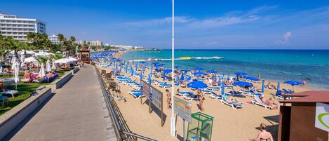 A beach with rows of sun loungers and umbrellas, a boardwalk, and a clear view of the ocean.