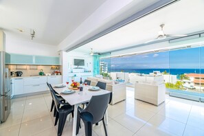 A modern kitchen with white cabinets, a dining area with a table and chairs, and a large balcony with a view of the ocean. - Silver Sands Penthouse (Paralimni)