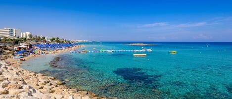 A beach with clear turquoise water, rocky shoreline, and blue umbrellas.