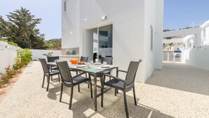 Uma área de refeições moderna ao ar livre, com uma mesa posta para quatro pessoas, rodeada por cadeiras de vime.