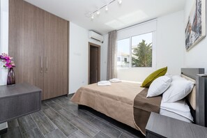 A modern hotel room with a bed, a desk, and a wardrobe. - Green Bay Villa 15 in Protaras (Paralimni)