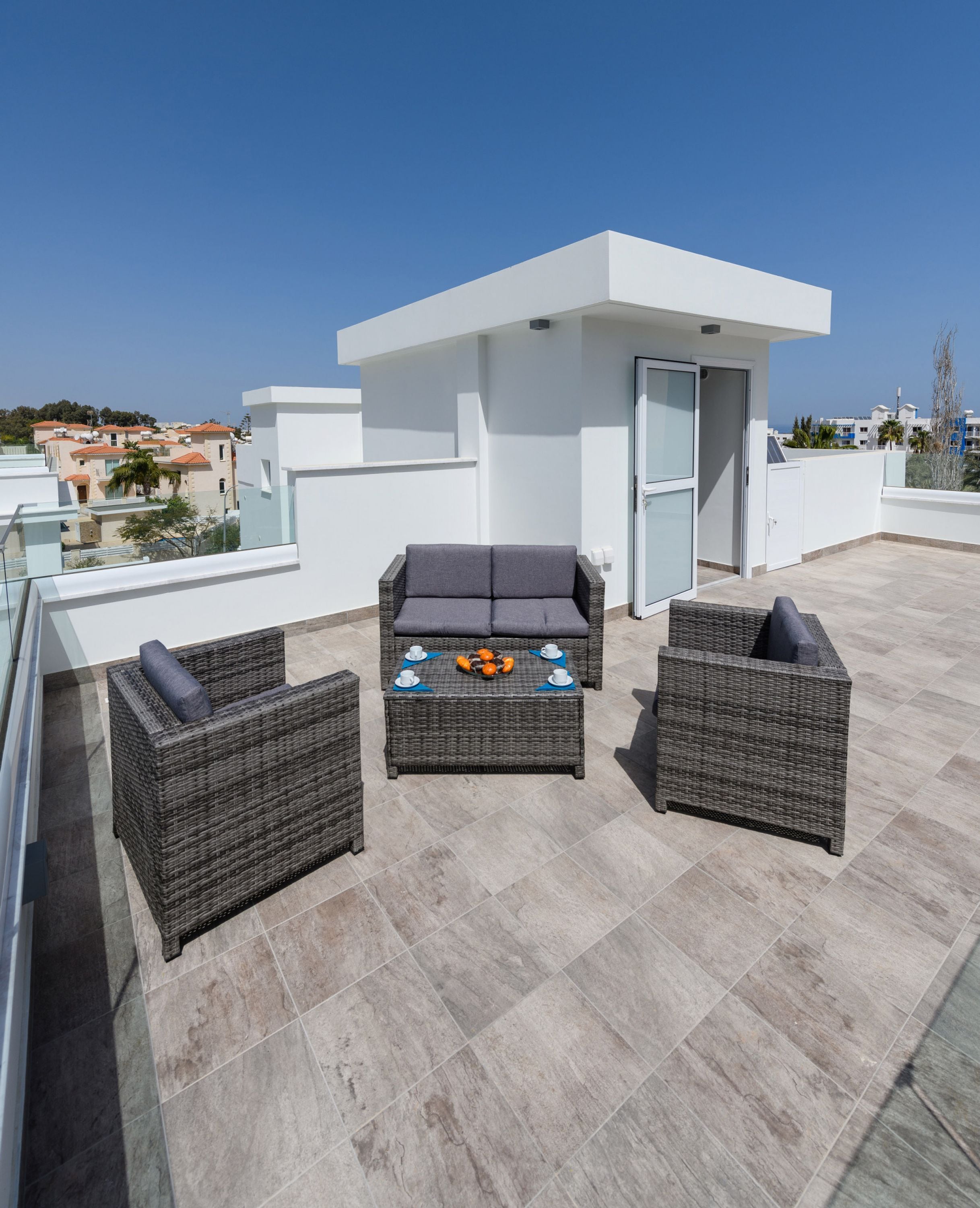 Eine Dachterrasse mit Korbmöbeln, einem kleinen Tisch mit Früchten und Blick auf die Stadtlandschaft.