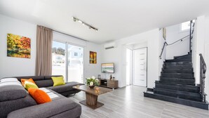 Uma sala de estar moderna com um sofá seccional cinza, uma mesa de centro de madeira e uma escada que leva a um andar superior.