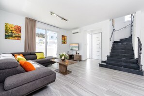 Una sala de estar moderna con un sofá seccional gris, una mesa de centro de madera y una escalera que sube a un piso superior.