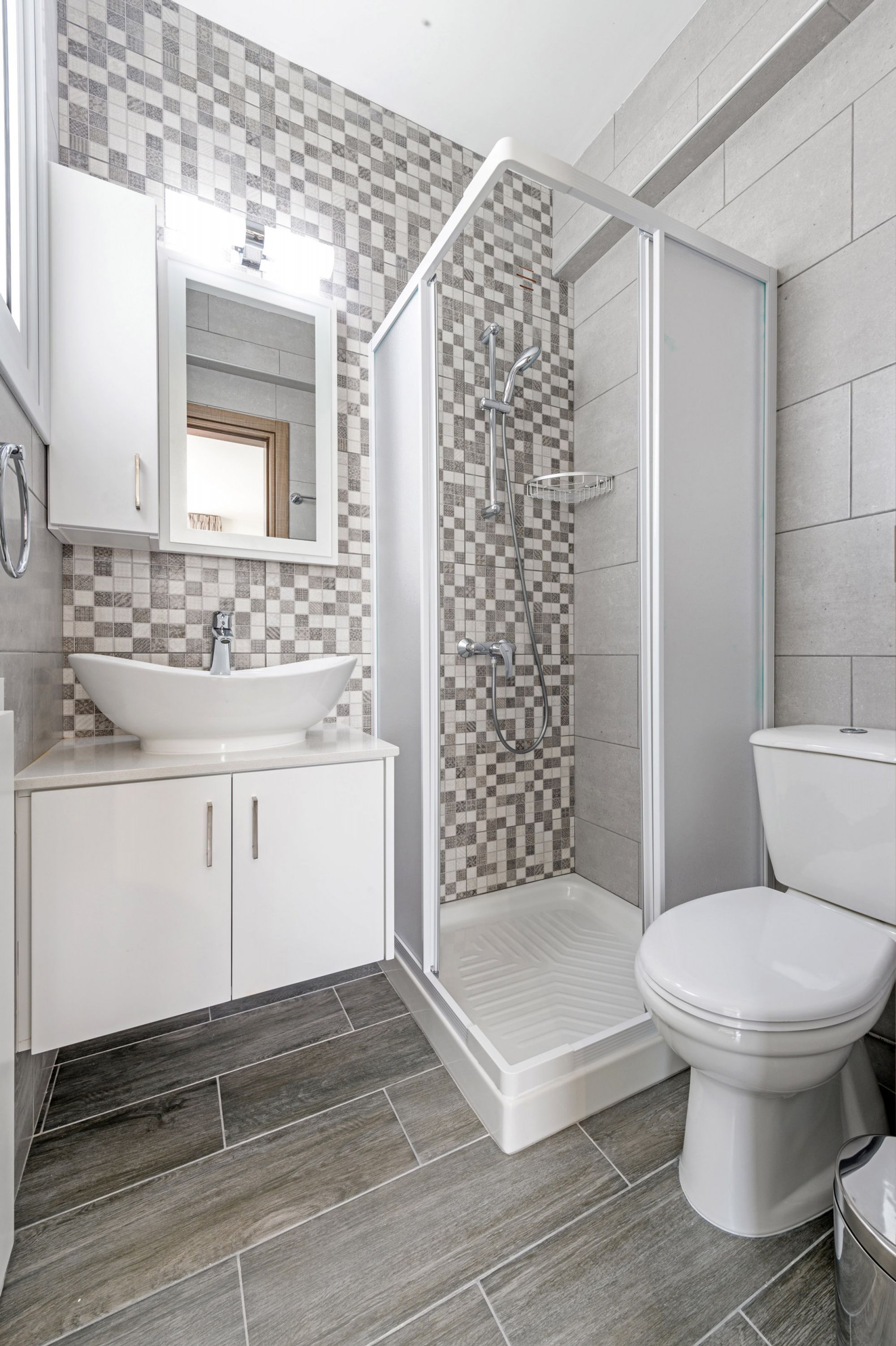 Een moderne badkamer met een betegelde spatwand in ruitpatroon, een wit wastafelmeubel, een douche met glazen wanden en een toilet.