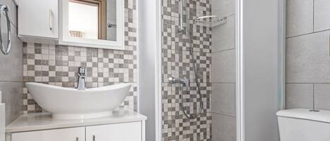 Een moderne badkamer met een betegelde spatwand in ruitpatroon, een wit wastafelmeubel, een douche met glazen wanden en een toilet.