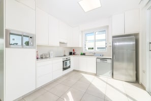 A modern kitchen with white cabinetry, a built-in oven, a dishwasher, and a stainless steel refrigerator. - Green Bay Villa 17 in Protaras (Paralimni)