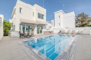 A modern building with a swimming pool, outdoor seating, and a clear sky. - Green Bay Villa 17 in Protaras (Paralimni)