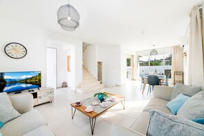 A spacious living room with a television, sofa, coffee table, and a view of a mountain lake through a large window. - Green Bay Villa 17 in Protaras (Paralimni)