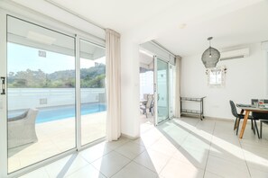 A spacious room with a large sliding glass door leading to a balcony with a pool view. - Green Bay Villa 17 in Protaras (Paralimni)