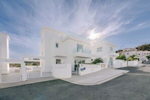 A modern white villa with a glass balcony, a driveway, and a clear sky. - Green Bay Villa 17 in Protaras (Paralimni)