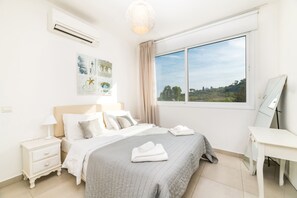 A bedroom with a bed, bedside tables, a desk, a window with a view, and wall art. - Green Bay Villa 17 in Protaras (Paralimni)