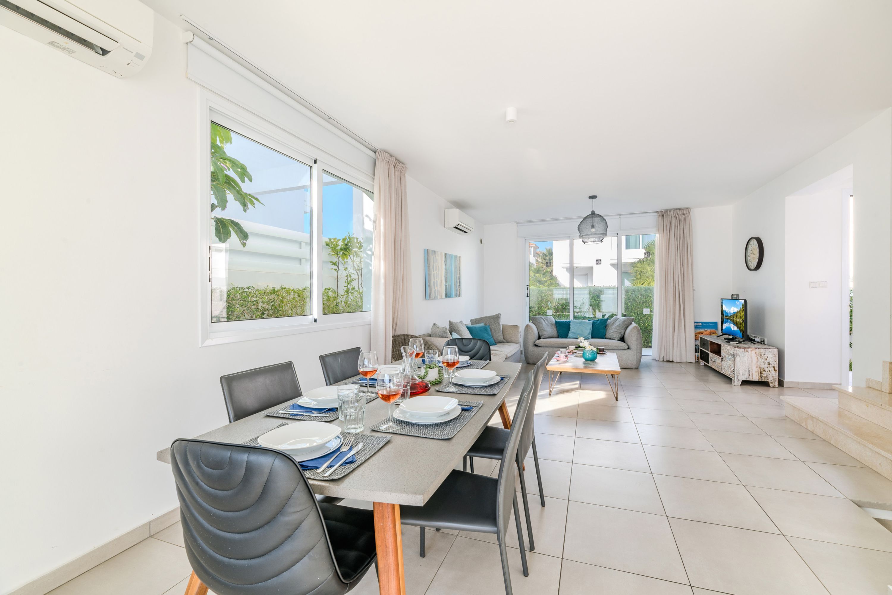 A modern dining area with a long table, chairs, and a view of the outdoors.