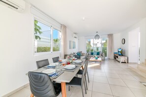 A modern dining area with a long table, chairs, and a view of the outdoors. - Green Bay Villa 17 in Protaras (Paralimni)