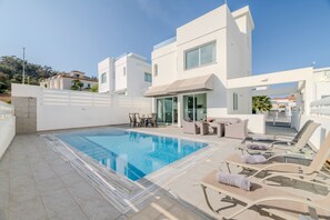 A modern pool area with lounge chairs and a dining set. - Green Bay Villa 17 in Protaras (Paralimni)