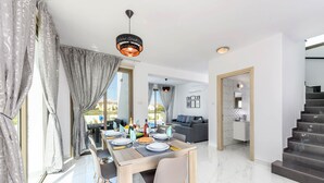 A modern dining area with a wooden table, chairs, and a hanging light fixture. - Villa Levanda 40 in Protaras (Paralimni)