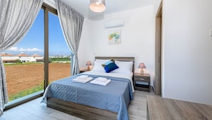 A bedroom with a large bed, a view of the countryside, and a modern pendant light. - Villa Levanda 40 in Protaras (Paralimni)