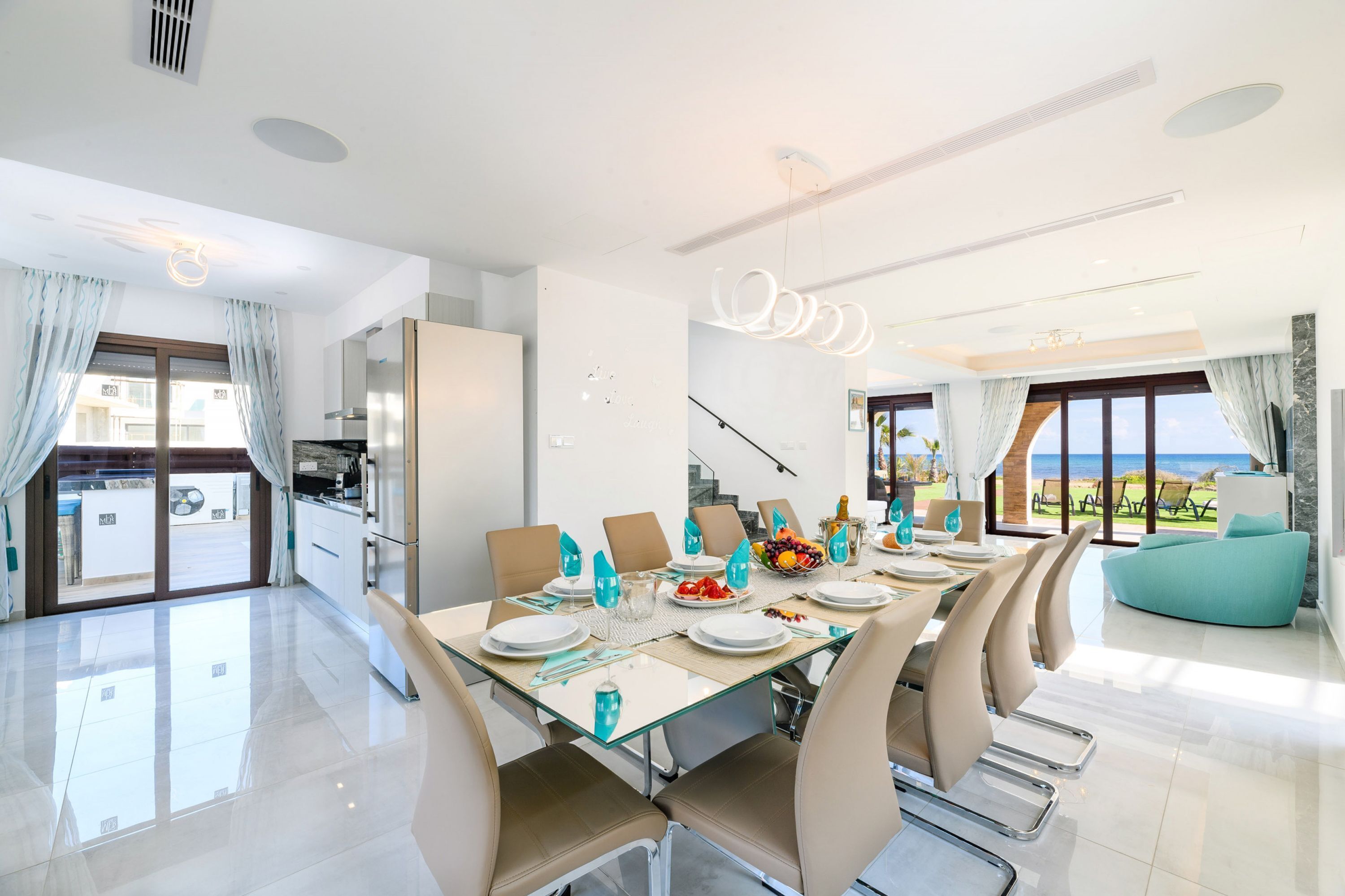 Un comedor moderno con una mesa de vidrio, sillas color beige y vista al mar.