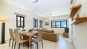 A modern living room with a dining area, a sofa, a TV, and a wooden shelf with decorative items. - Protaras Centro Villa (Paralimni)