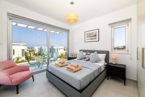 Un dormitorio moderno con una cama grande, un sillón rosa y un balcón con vistas a edificios.