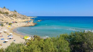 Una playa con aguas azules cristalinas, orillas de arena y afloramientos rocosos.